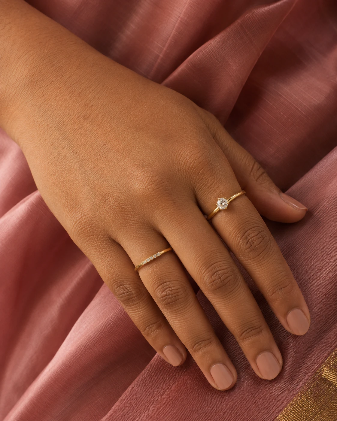 AI-generated close-up of gold rings on a hand resting on rose-colored saree fabric